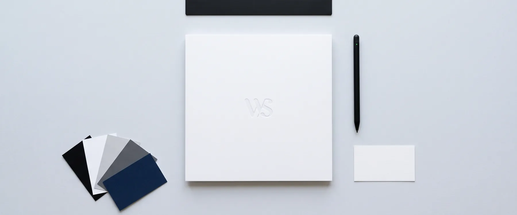 Une carte blanche gaufrée du monogramme WS, des nuanciers noir, blanc, gris et bleu nuit, un crayon et une règle